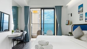 A hotel room with a bed, a desk, a chair, and a balcony with curtains. - Atermis Regency Hillside Phu Quoc - Sea & Fireworks View (Phu Quoc)