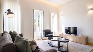 A modern living room with a sofa, a chair, a coffee table, a TV, and a lamp. - Caldeireiros 95 | Charming Home (Porto)