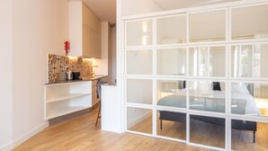A modern bedroom with a large window, a bed, and a kitchen area with a patterned backsplash. - Caldeireiros 95 | Charming Home (Porto)