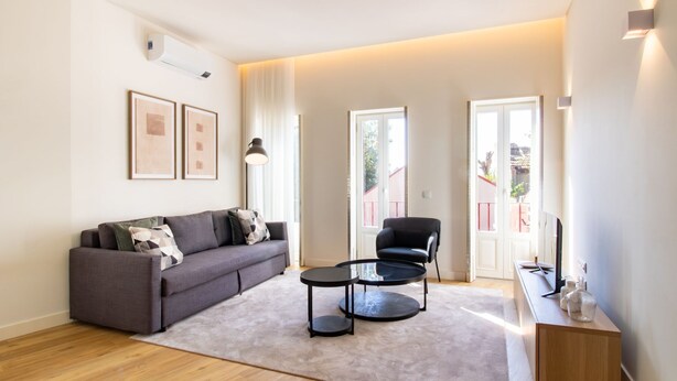 A modern living room with a grey sofa, two black chairs, a round coffee table, and a TV on a wooden cabinet. - Caldeireiros 95 | Charming Home (Porto)
