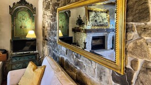 A cozy room with a stone wall, a large mirror, a fireplace, and a sofa with cushions. - La Fonte - Two Bedroom House, Sleeps 4 (Subbiano)