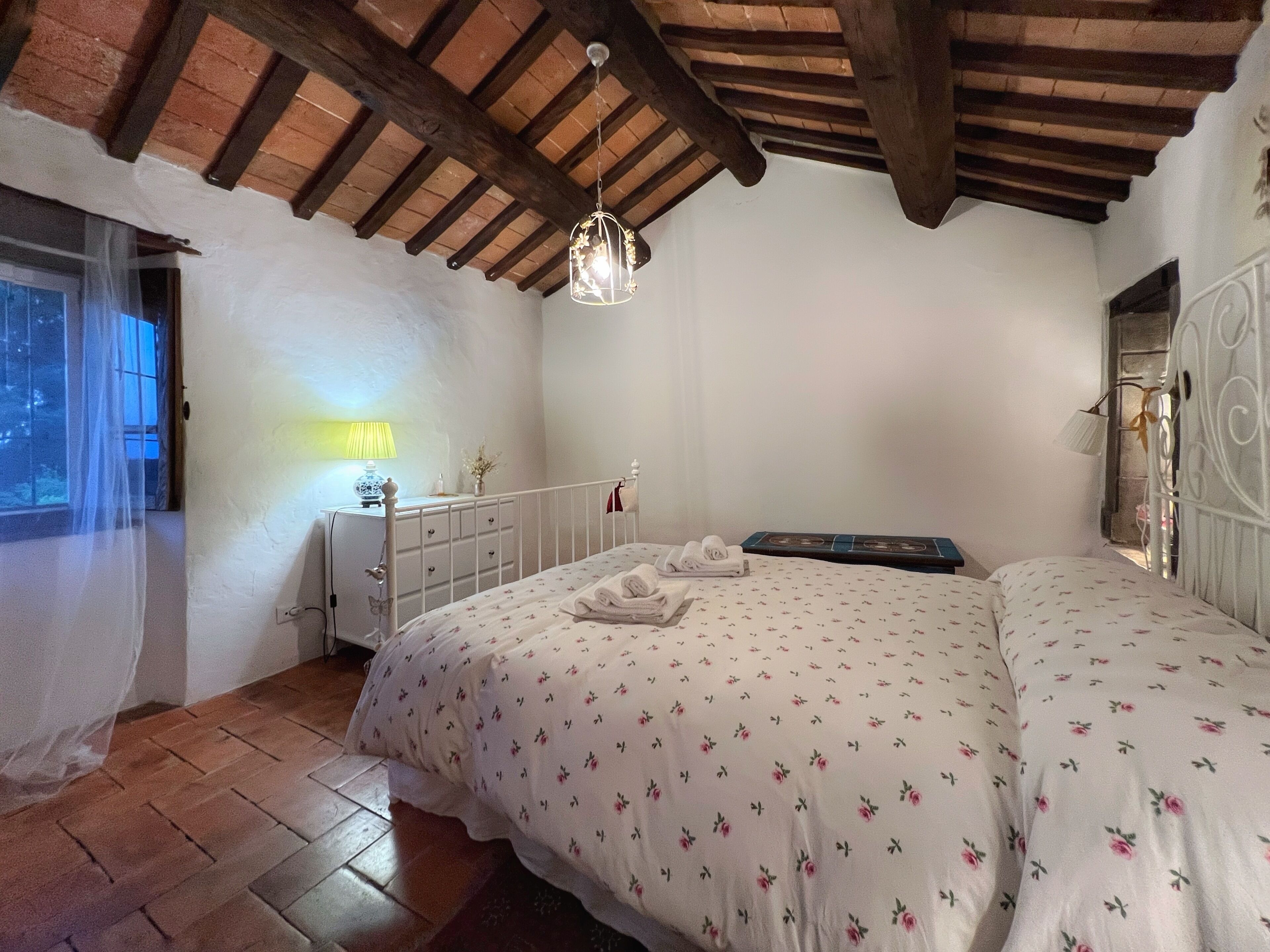 Een slaapkamer met een bed, nachtkastje, lamp en raam met gordijnen.