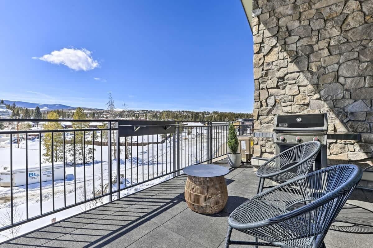 Un balcon avec des murs en pierre, un barbecue, deux fauteuils en osier et une table ronde.