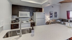Una cocina moderna con armarios oscuros, encimera blanca, electrodomésticos de acero inoxidable y una zona de comedor con sofá y mesa.
