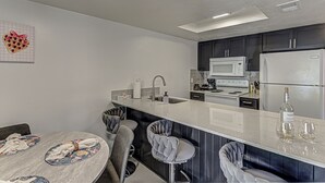 Una cocina moderna con armarios oscuros, encimera blanca y una isla central con taburetes de bar.