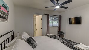 Un dormitorio con una cama, un ventilador de techo, un televisor y una puerta que da a otra habitación.