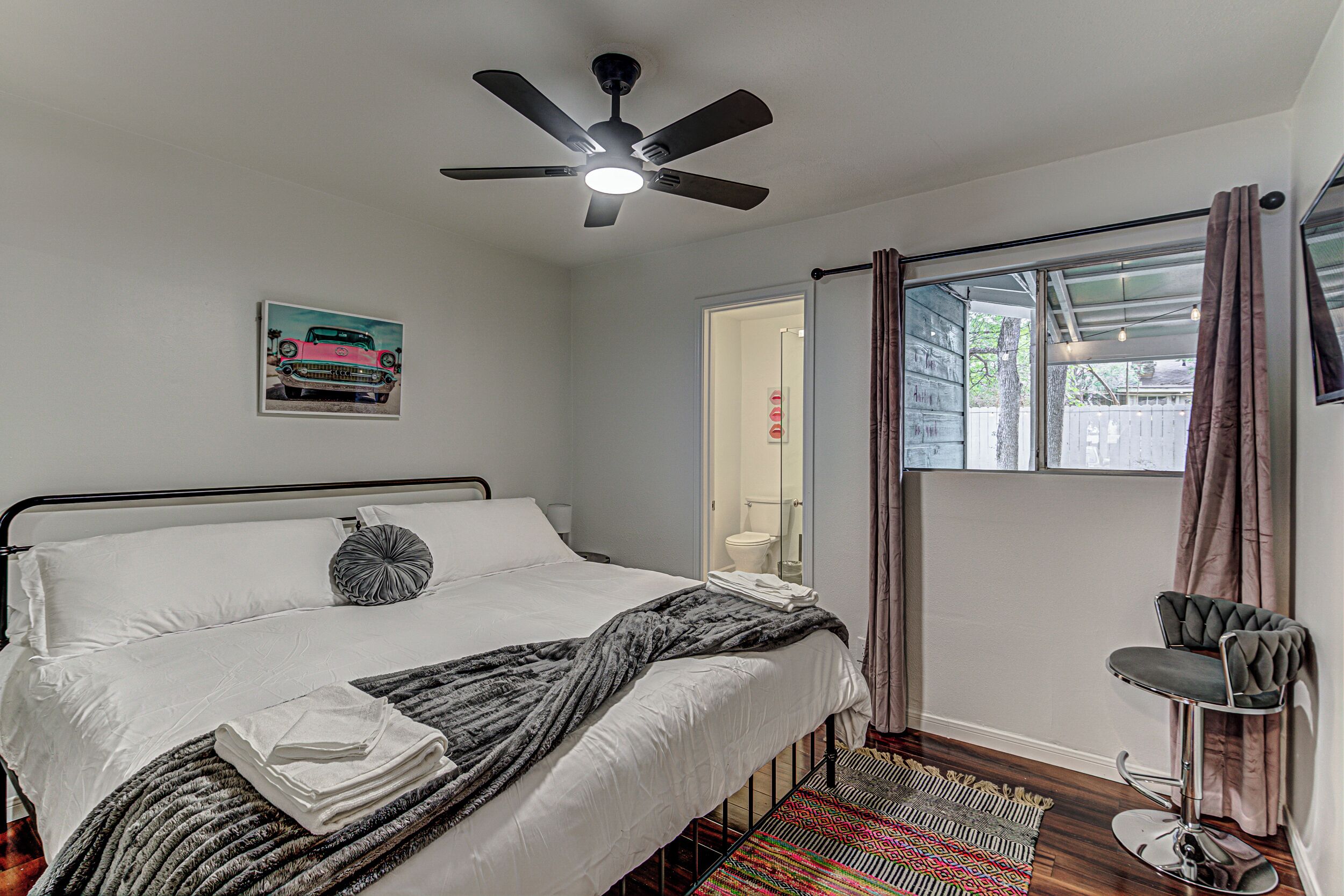 A bedroom with a bed, a ceiling fan, a window with curtains, and a chair.