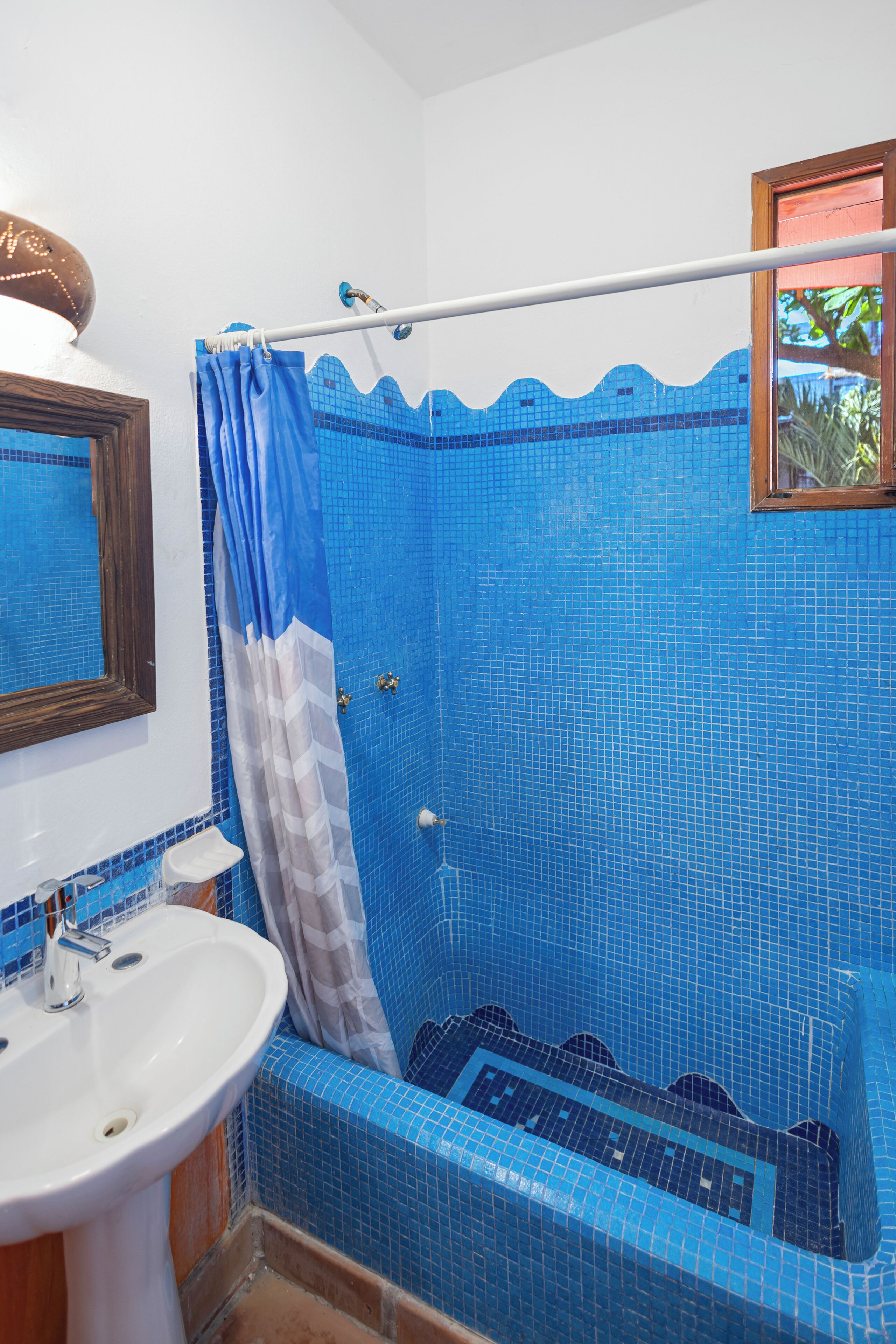 Un baño con ducha de azulejos azules, un lavabo blanco y un espejo con marco de madera.
