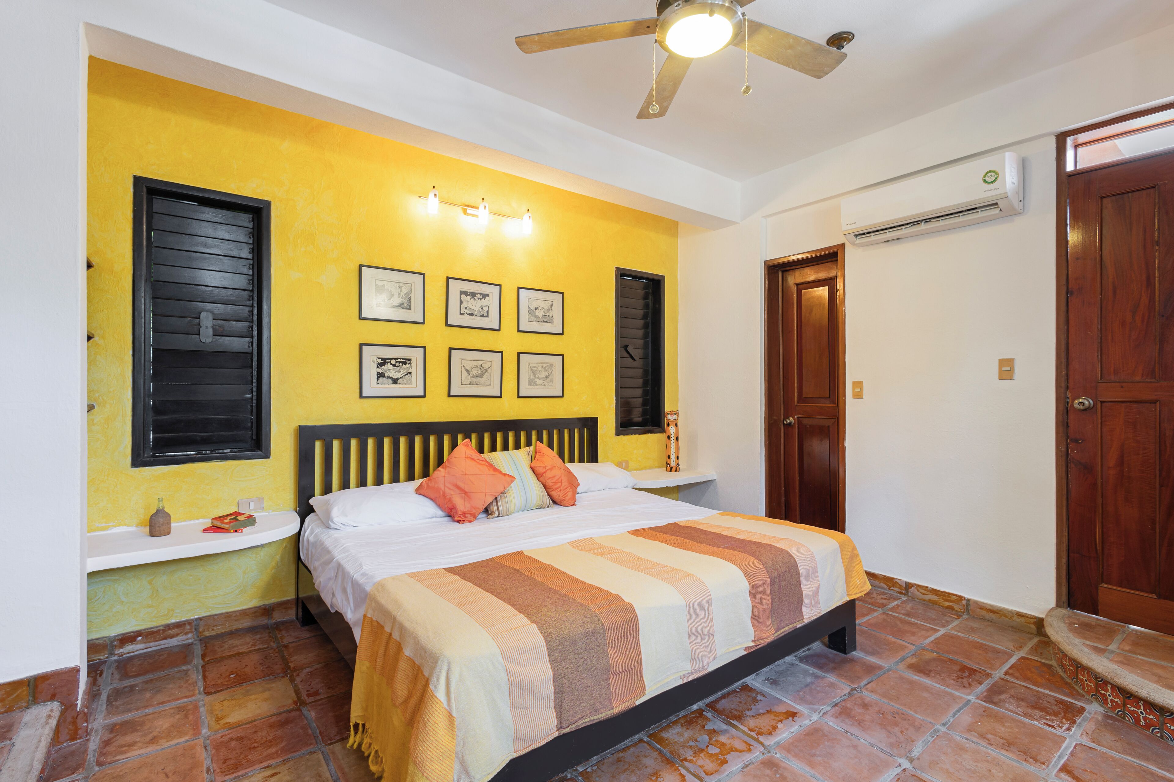 A bedroom with a bed, a ceiling fan, a wall-mounted air conditioner, and a door.
