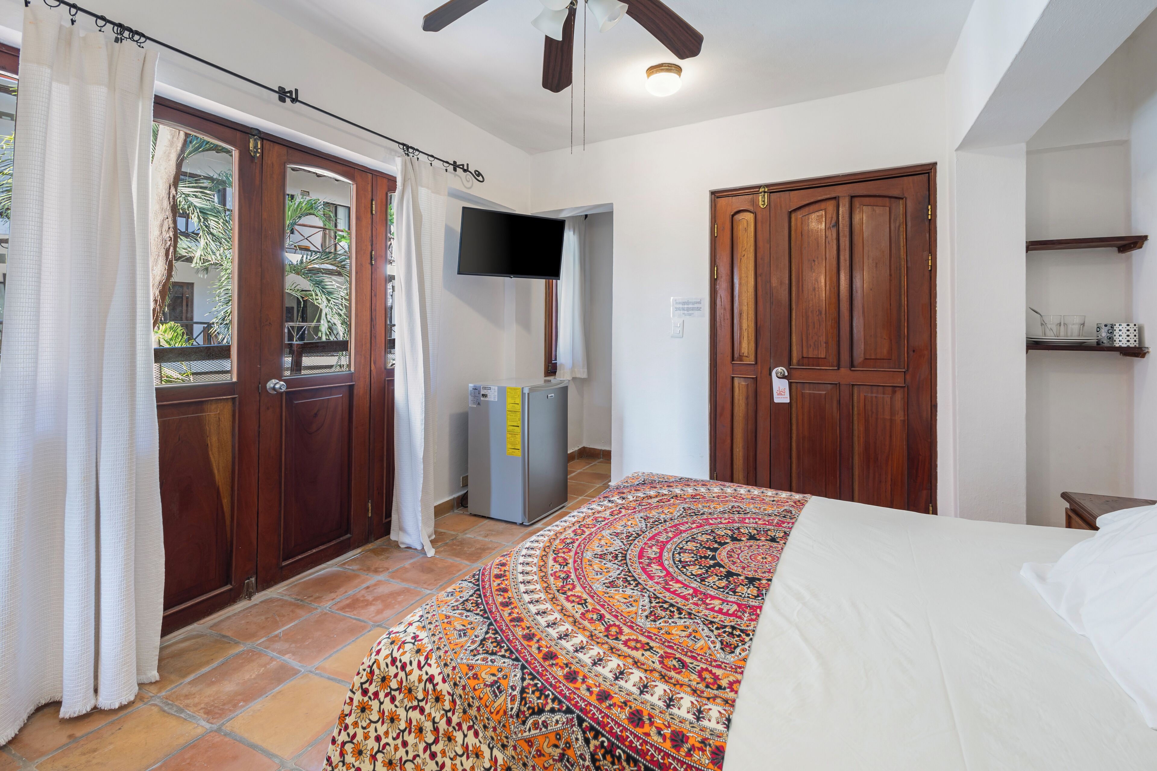 A bedroom with a bed, a television, a wardrobe, and a small refrigerator.