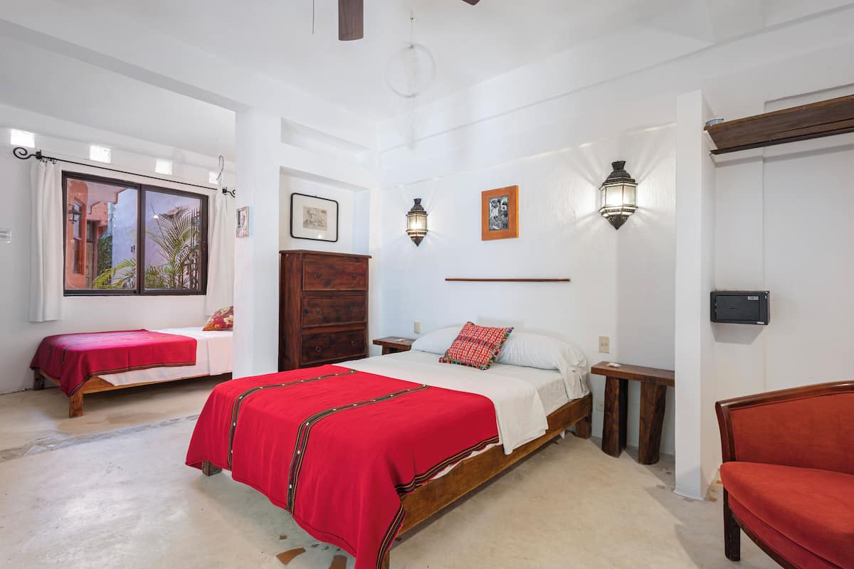 Een slaapkamer met twee bedden, een houten garderobe, een nachtkastje, een bankje en een wandlamp.