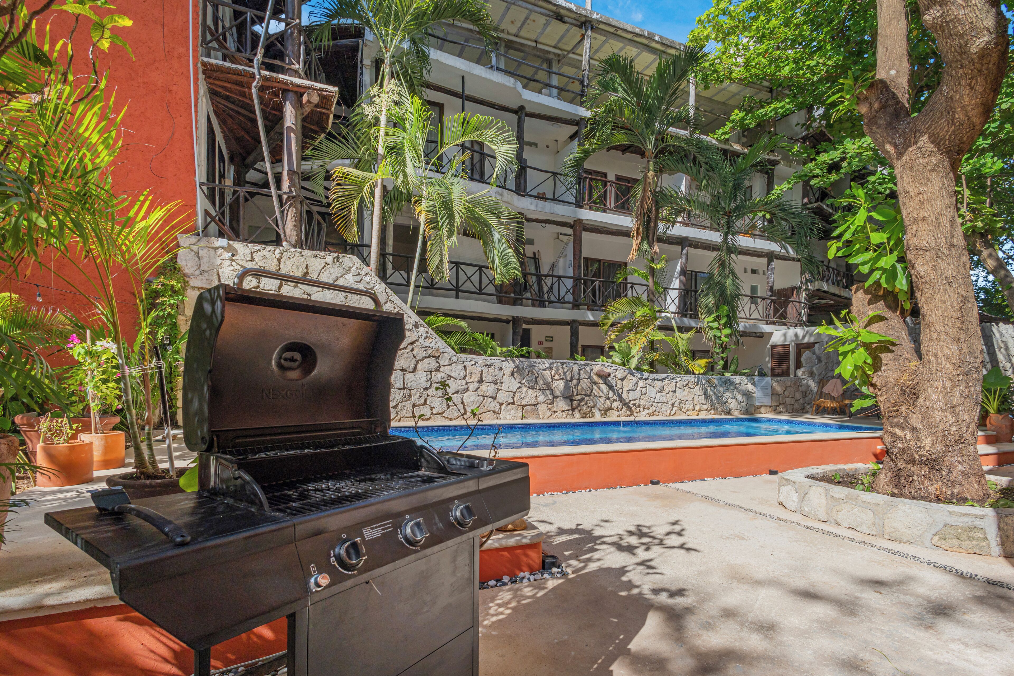 A barbecue grill in a courtyard with a pool and a multi-story building in the background.