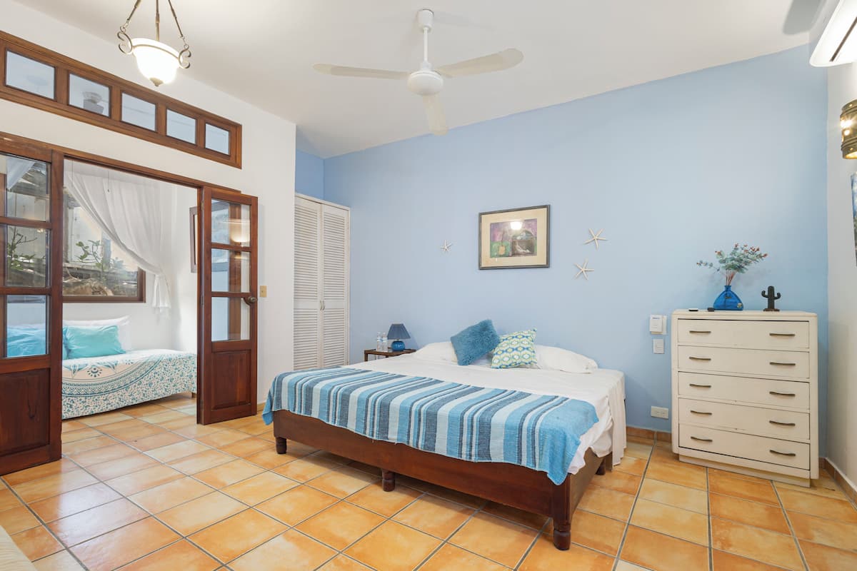 Een slaapkamer met een bed, een dressoir, een plafondventilator en een raam met gordijnen.