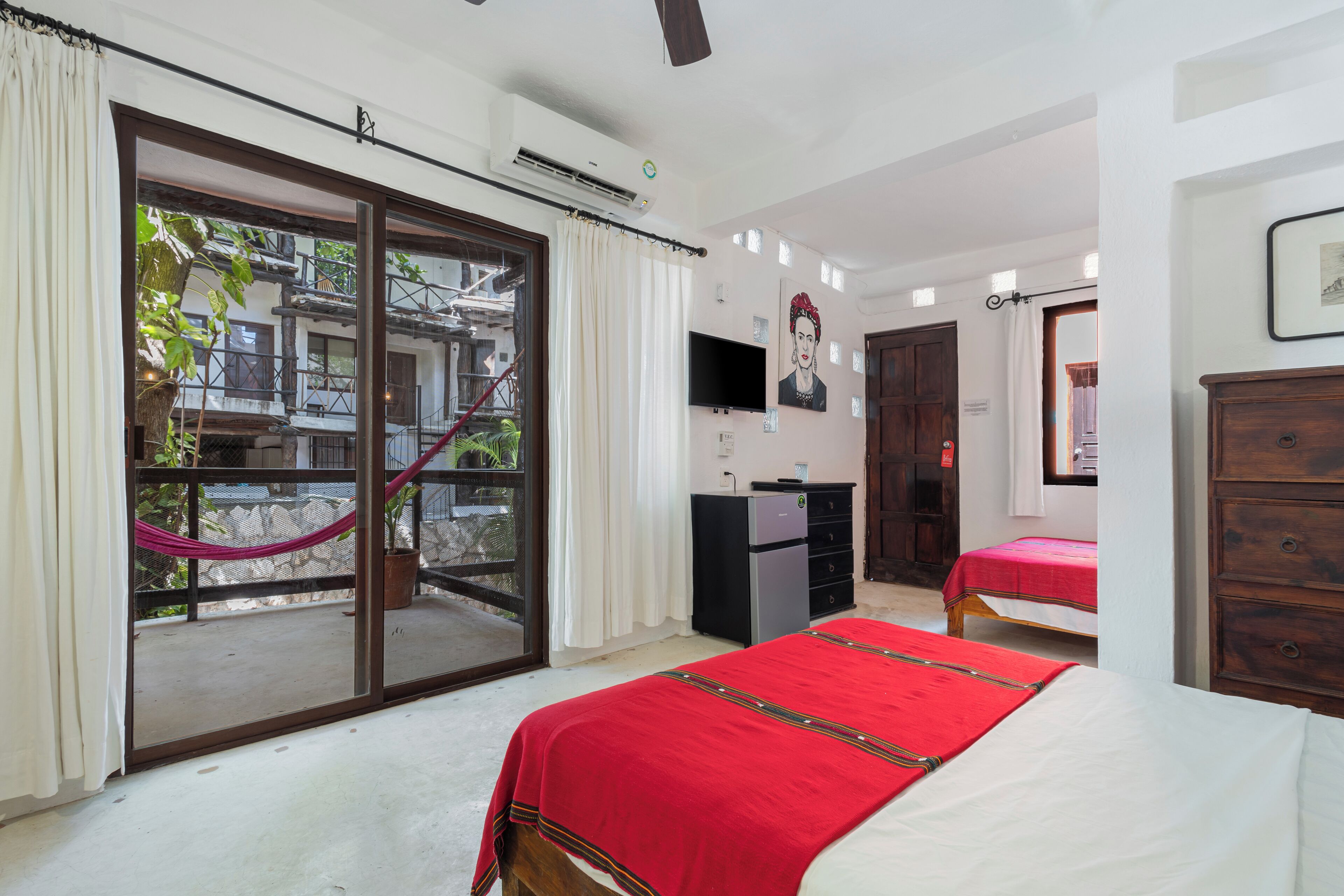 A hotel room with a bed, a desk, a TV, and a balcony with a hammock.
