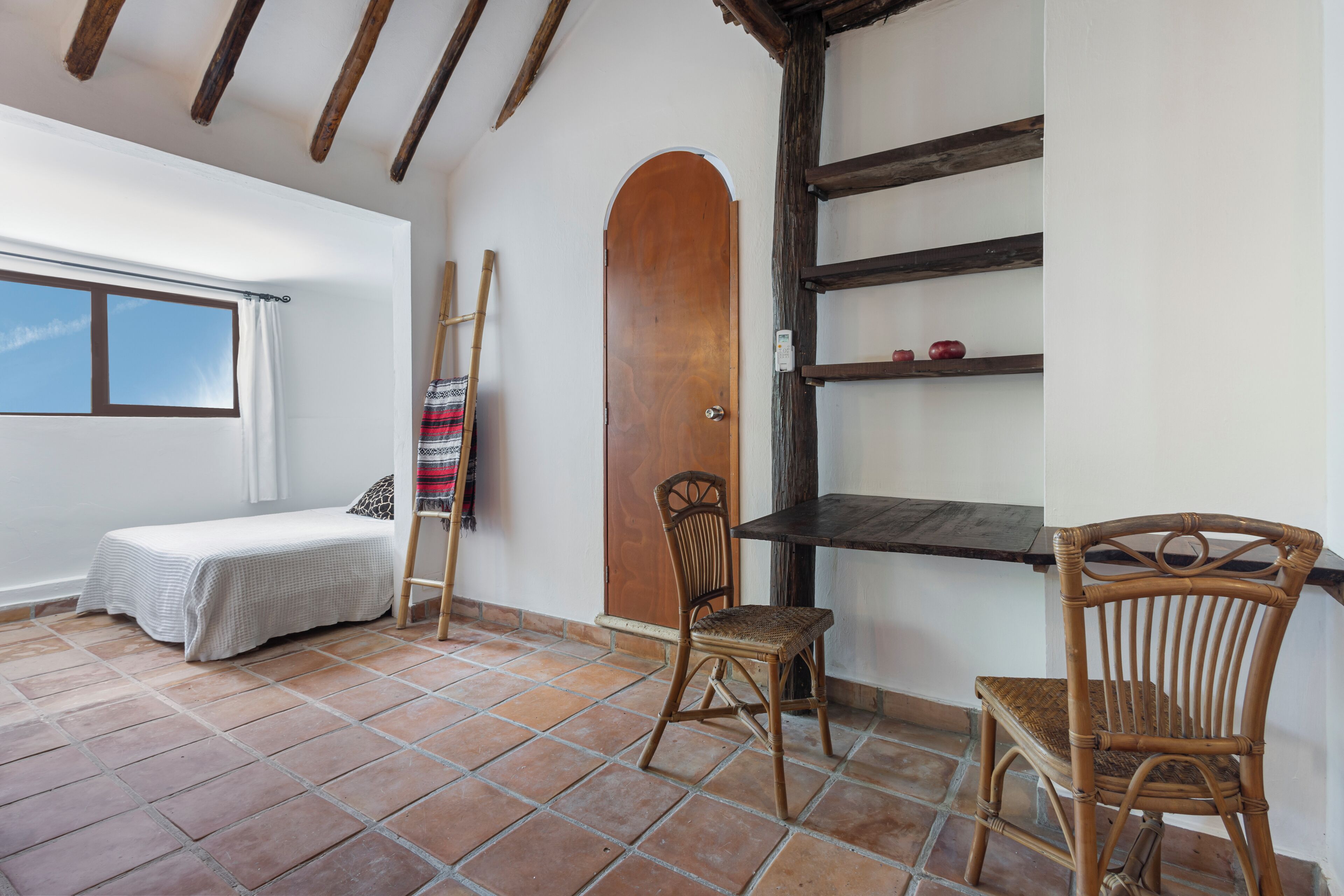 Une pièce comprenant un lit, deux fauteuils en osier, une porte en bois et une étagère avec une échelle.