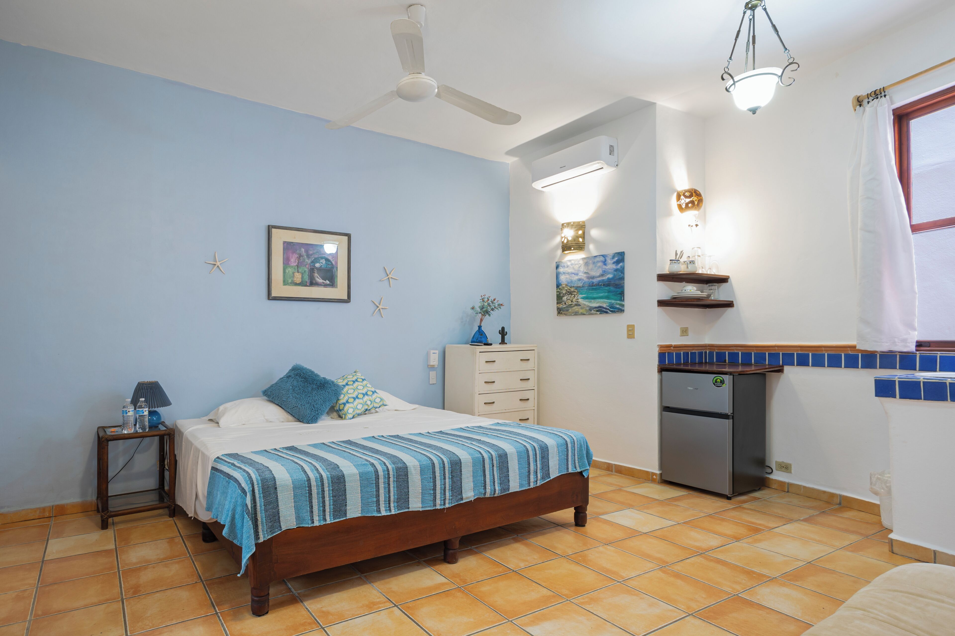 A bedroom with a bed, nightstand, dresser, and a small refrigerator.