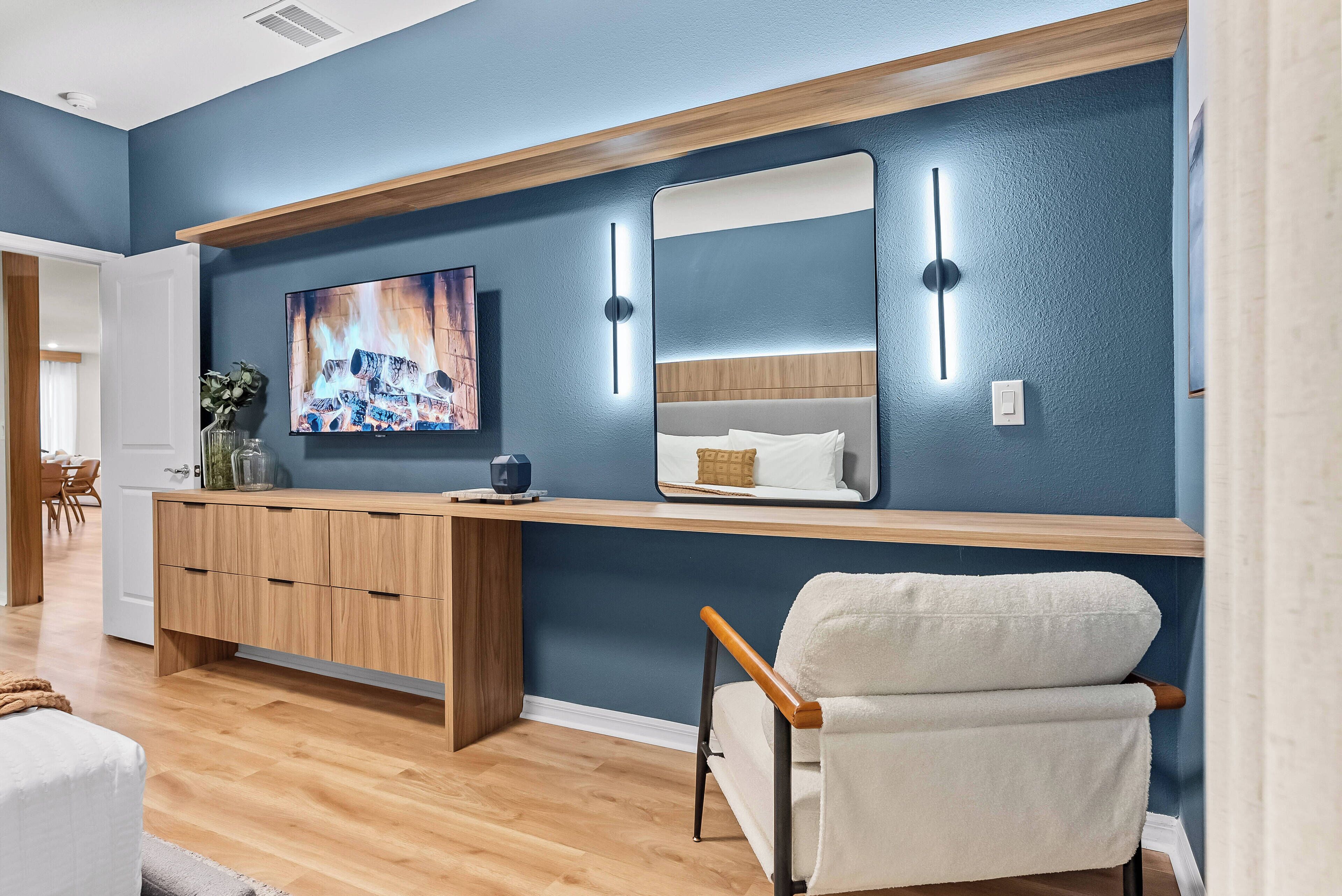 A modern bedroom with a large bed, a bedside table, a mirror, and a TV on the wall.