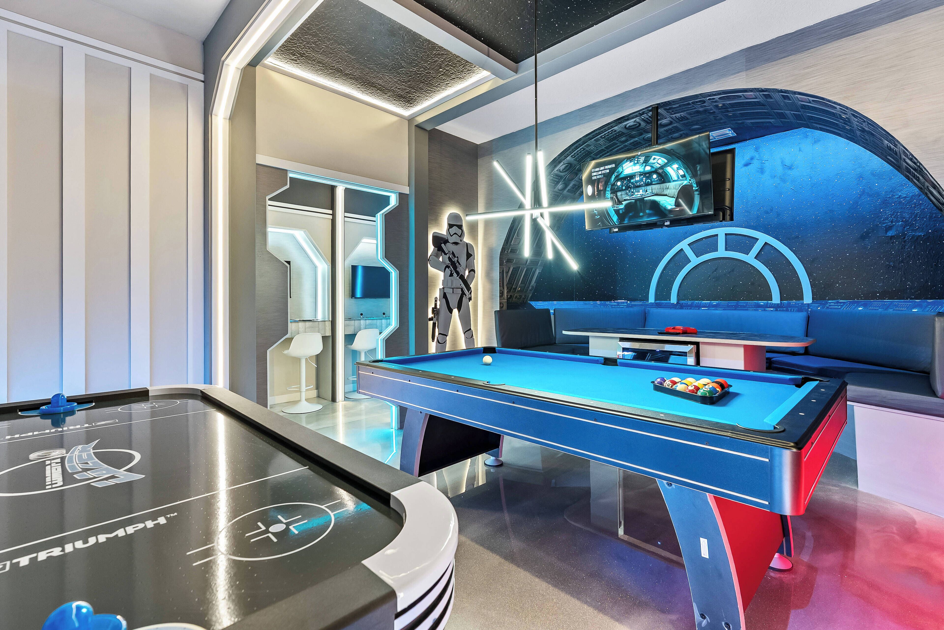 A pool table with a Star Wars theme, a pool cue, and a large screen displaying a game.