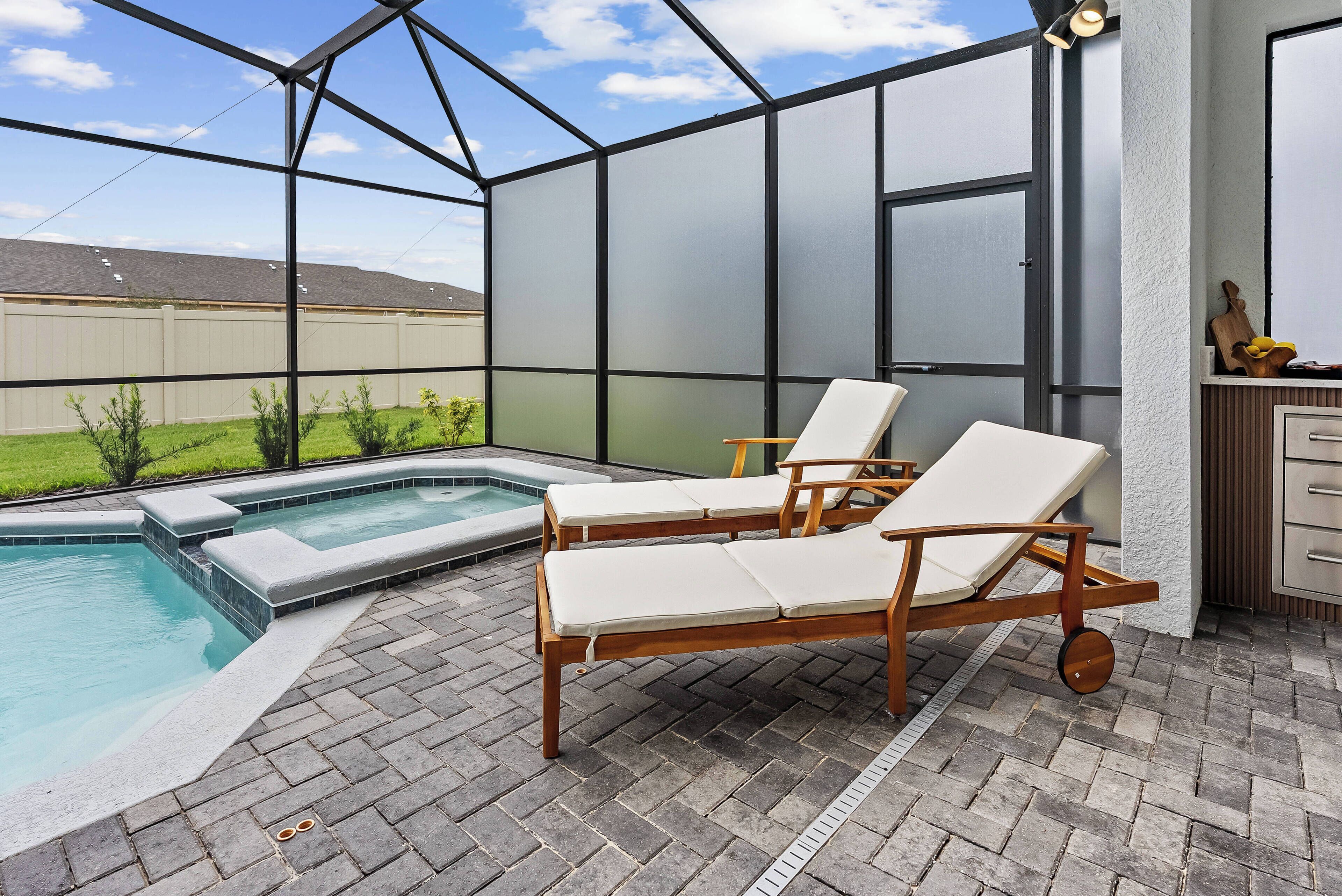 A covered outdoor area with a pool, lounge chairs, and a wooden table.