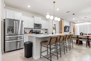 Cozinha moderna com eletrodomésticos de aço inoxidável, uma ilha central com banquetas e uma área de jantar com mesa e cadeiras.