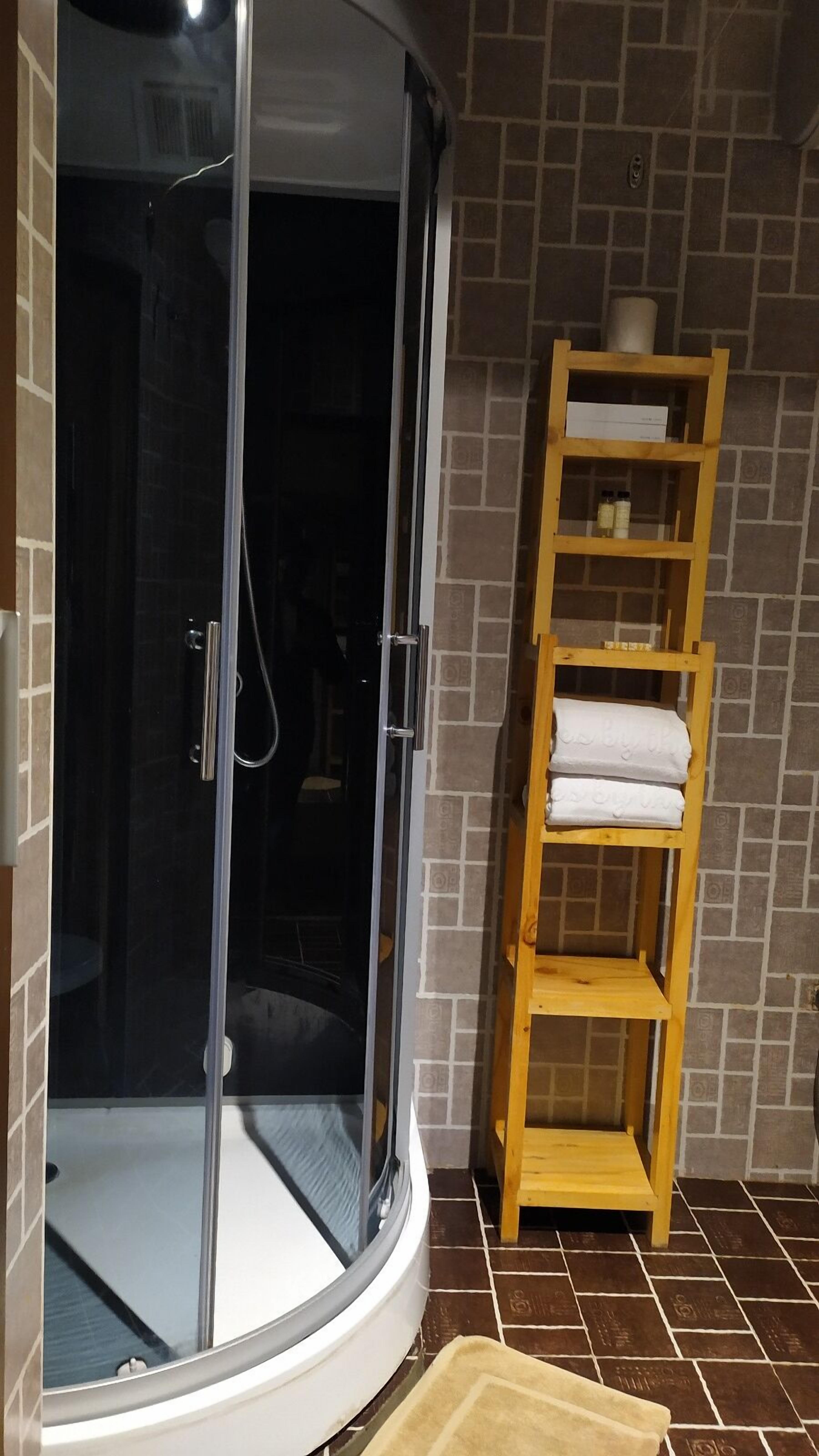 A glass-enclosed shower area with a wooden shelf holding towels.