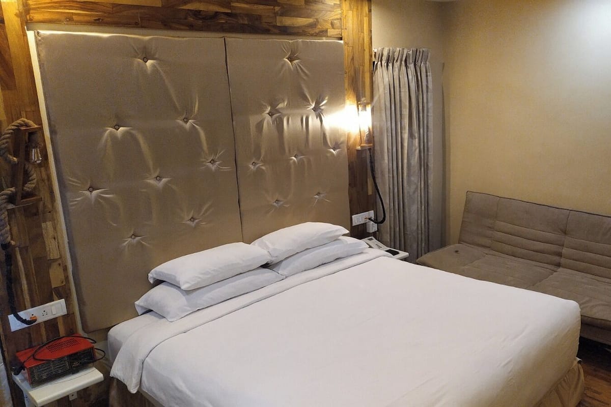 A bedroom with a large bed, a sofa, a wooden headboard, and a curtain.