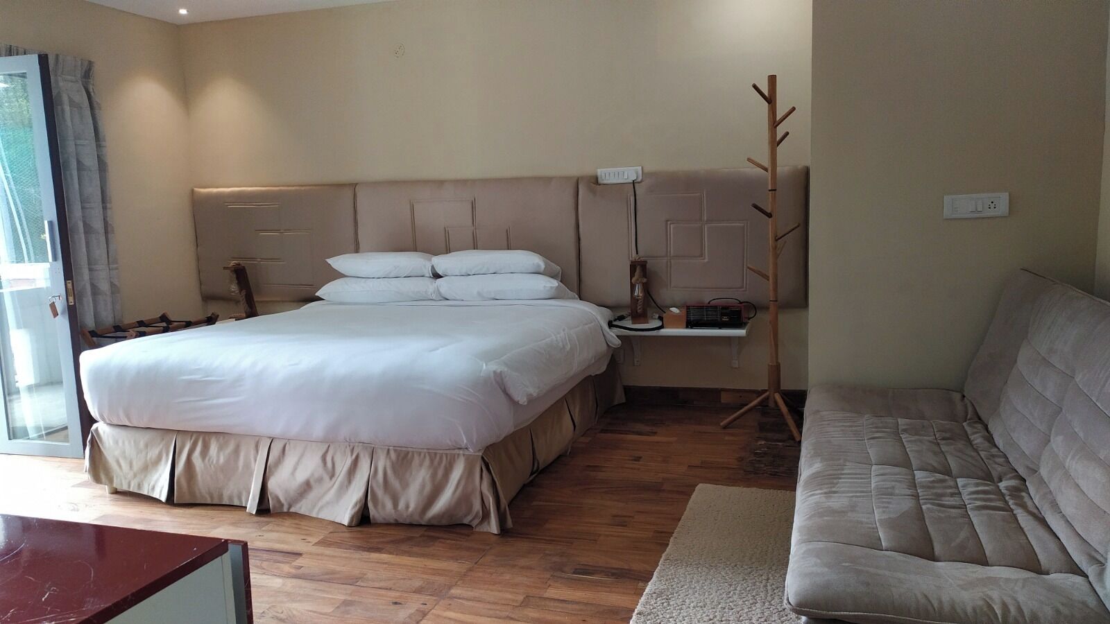 A bedroom with a large bed, bedside tables, a nightstand, a wooden coat rack, and a sofa.