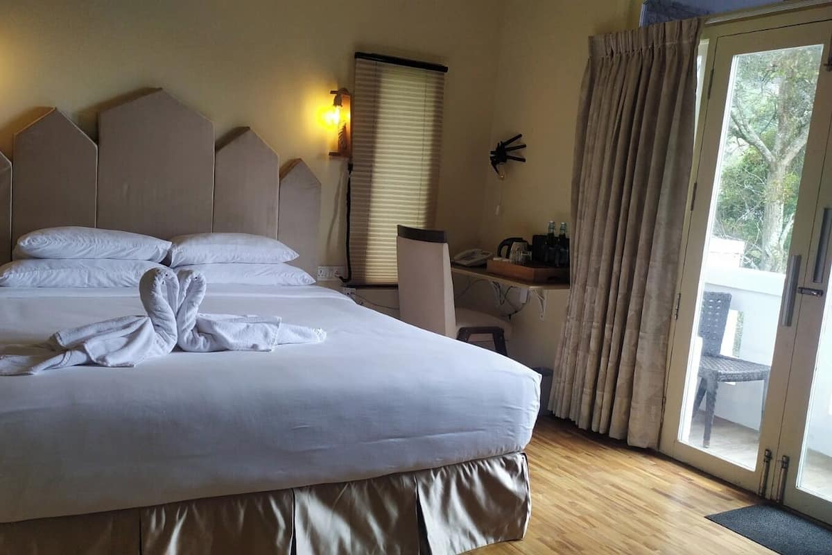 A neatly made bed with a towel arrangement, a desk with a chair, and a window with curtains.
