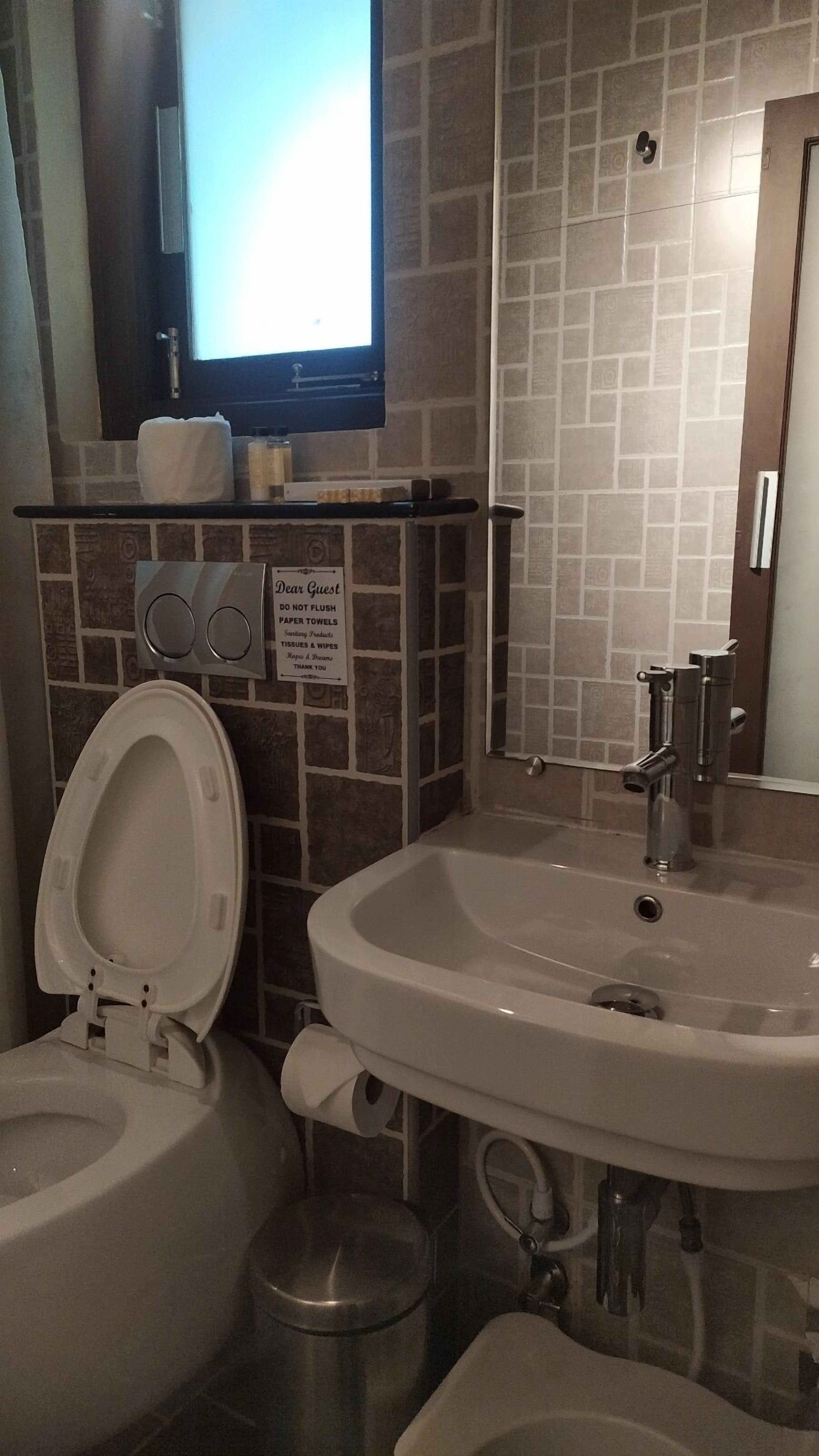 A bathroom with a toilet, bidet, and bathtub. There is a sign on the wall and a window above the toilet.