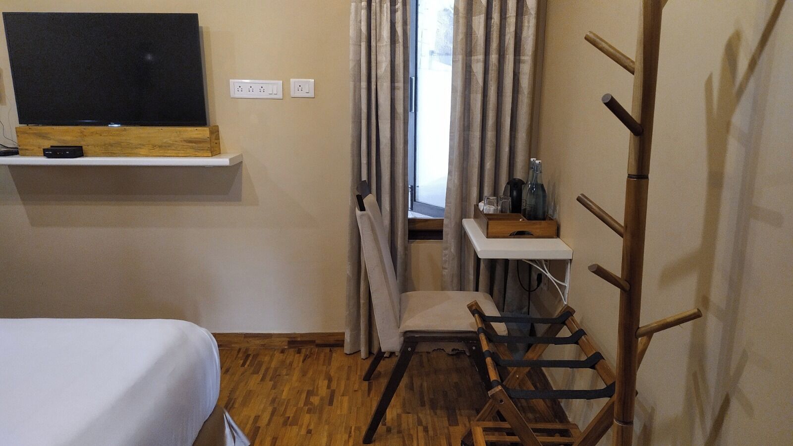 A compact hotel room with a bed, a small desk, a chair, and a wooden ladder.