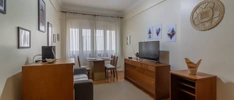 Una sala de estar con sofá, televisión, armarios de madera, una mesa de comedor con sillas y un ventilador de techo.