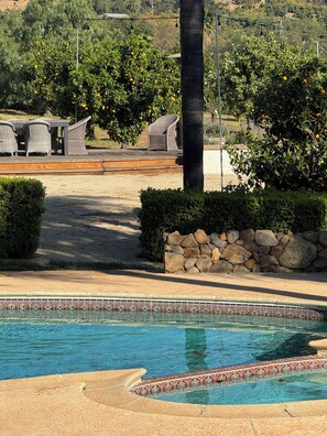 A pool area with a tiled edge, a stone wall, and a seating area with chairs and a table.