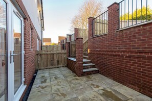 A brick exterior with a wooden fence, a metal gate, and a staircase leading to a higher level. - Toast Stays - Dene Edge (Lanchester)
