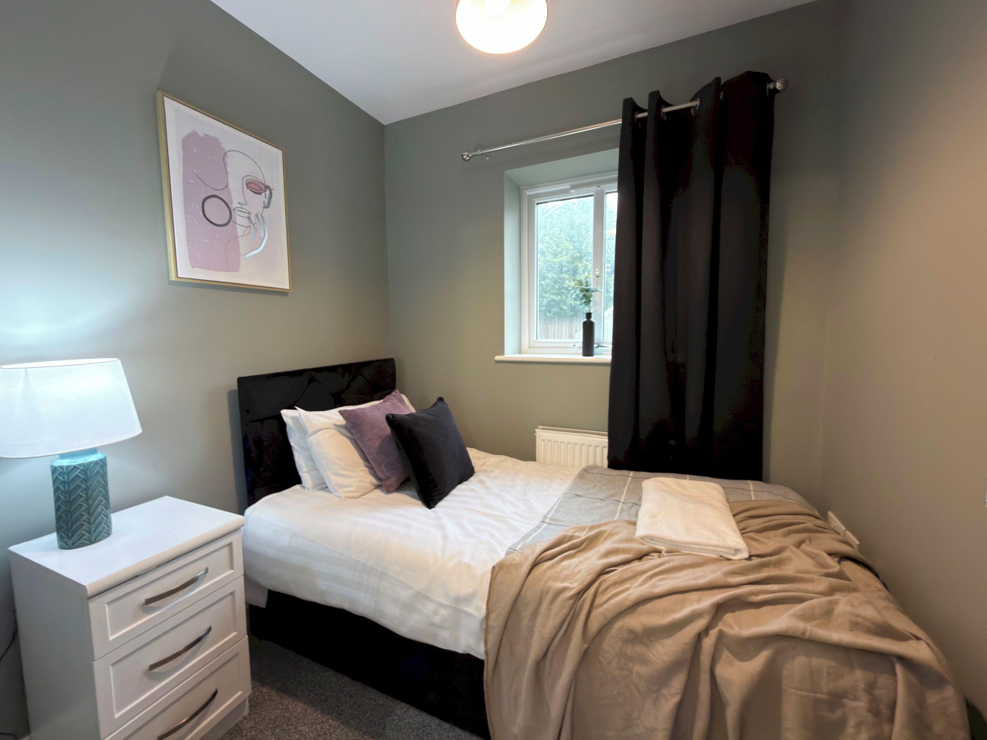 A bedroom with a bed, bedside table, lamp, and a window with curtains.