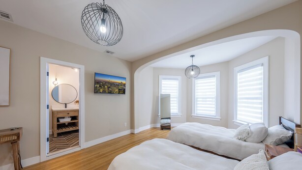 A bedroom with two beds, wooden flooring, a desk, and a cityscape painting. - Casa Francesca 6BR Villa & Heated Pool (Roselle)