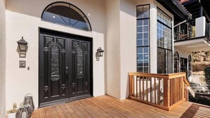 A wooden deck with a black double door and a balcony with a wooden railing. - Hilltop Villa_Amazing Pool+Views (Fallbrook)
