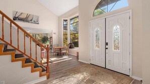A spacious interior with a wooden staircase, a dining area, and a large arched window. - Hilltop Villa_Amazing Pool+Views (Fallbrook)