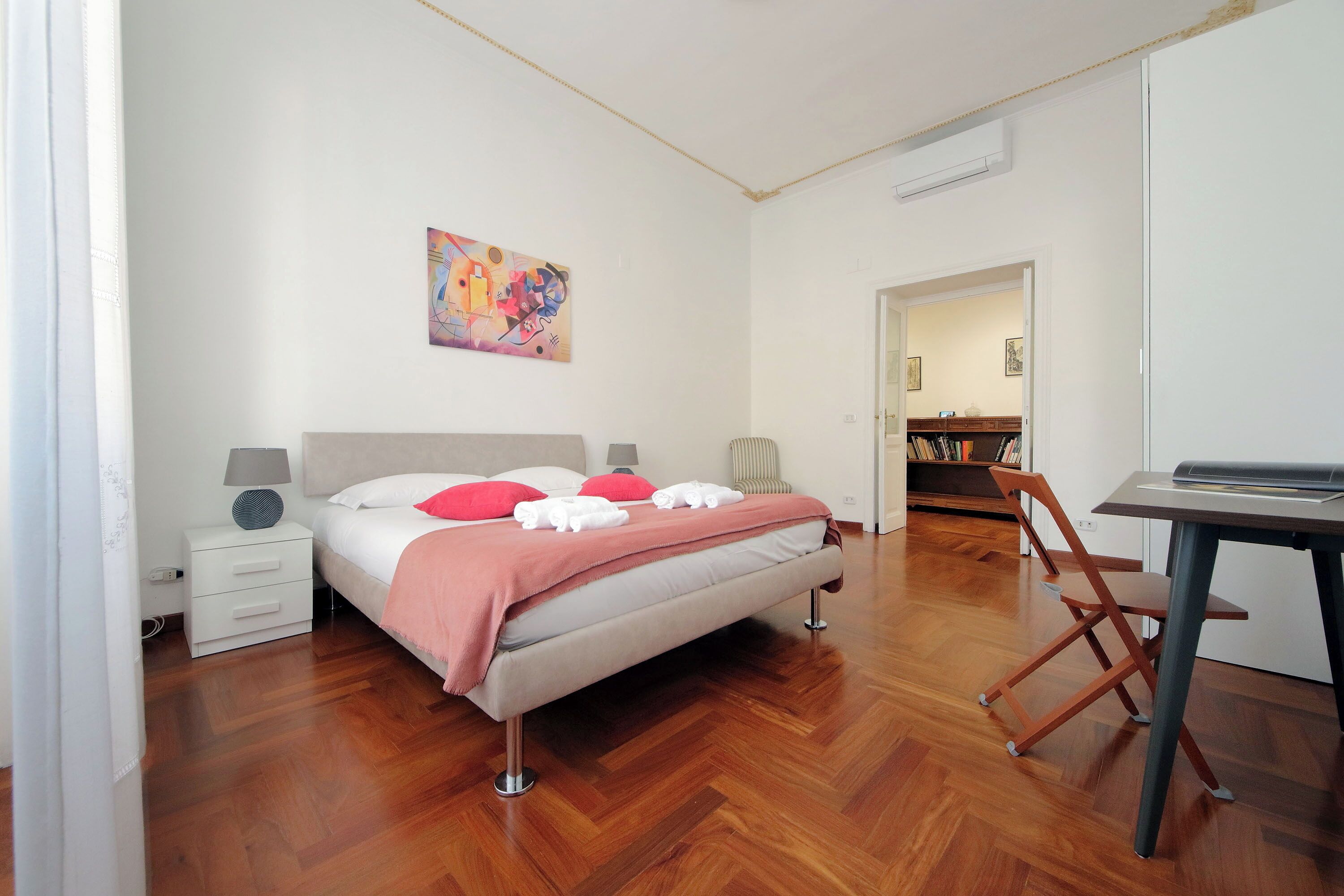 Un dormitorio con cama, mesita de noche, lámpara y un cuadro en la pared.
