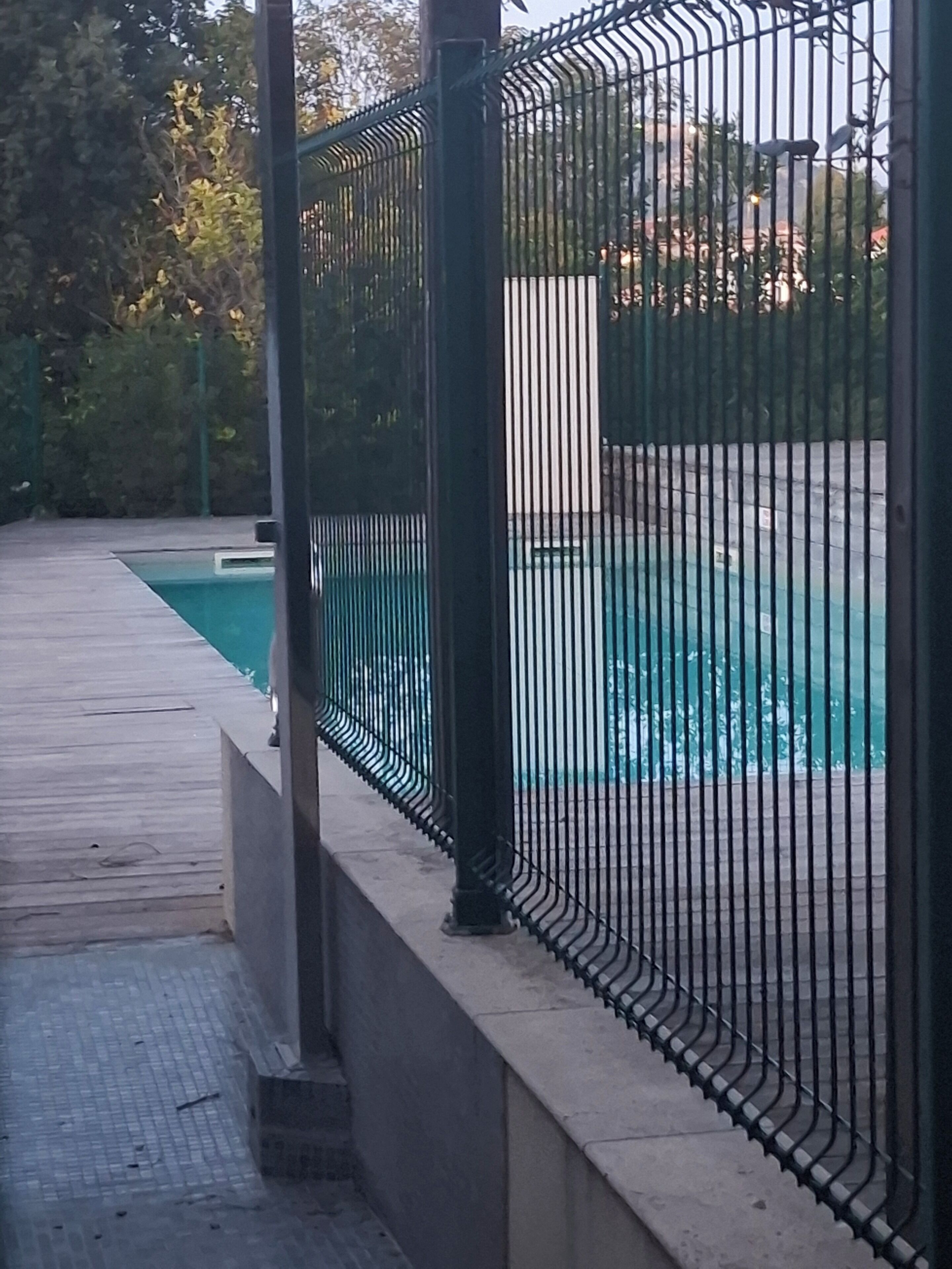 A swimming pool with a metal fence, a concrete deck, and a paved walkway.