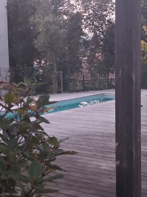A wooden deck with a swimming pool, surrounded by trees and a stone wall.