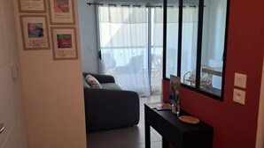 A living room with a sofa, a coffee table, and a large mirror. There are framed pictures on the wall and a sliding glass door leading to a balcony. - Quiet apartment near the beaches—relaxation guaranteed with air conditioning (Six-Fours-les-Plages)