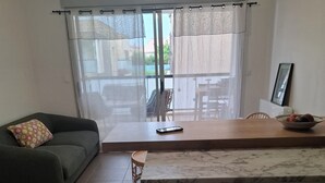 A modern living room with a sofa, a dining table, and a kitchen area. - Quiet apartment near the beaches—relaxation guaranteed with air conditioning (Six-Fours-les-Plages)