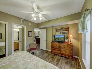 Ein Schlafzimmer mit einem Bett, einem Schminktisch, einem Fernseher und einem Deckenventilator.