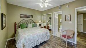 Un dormitorio con cama, una silla, ventilador de techo y una puerta que da a otra habitación.