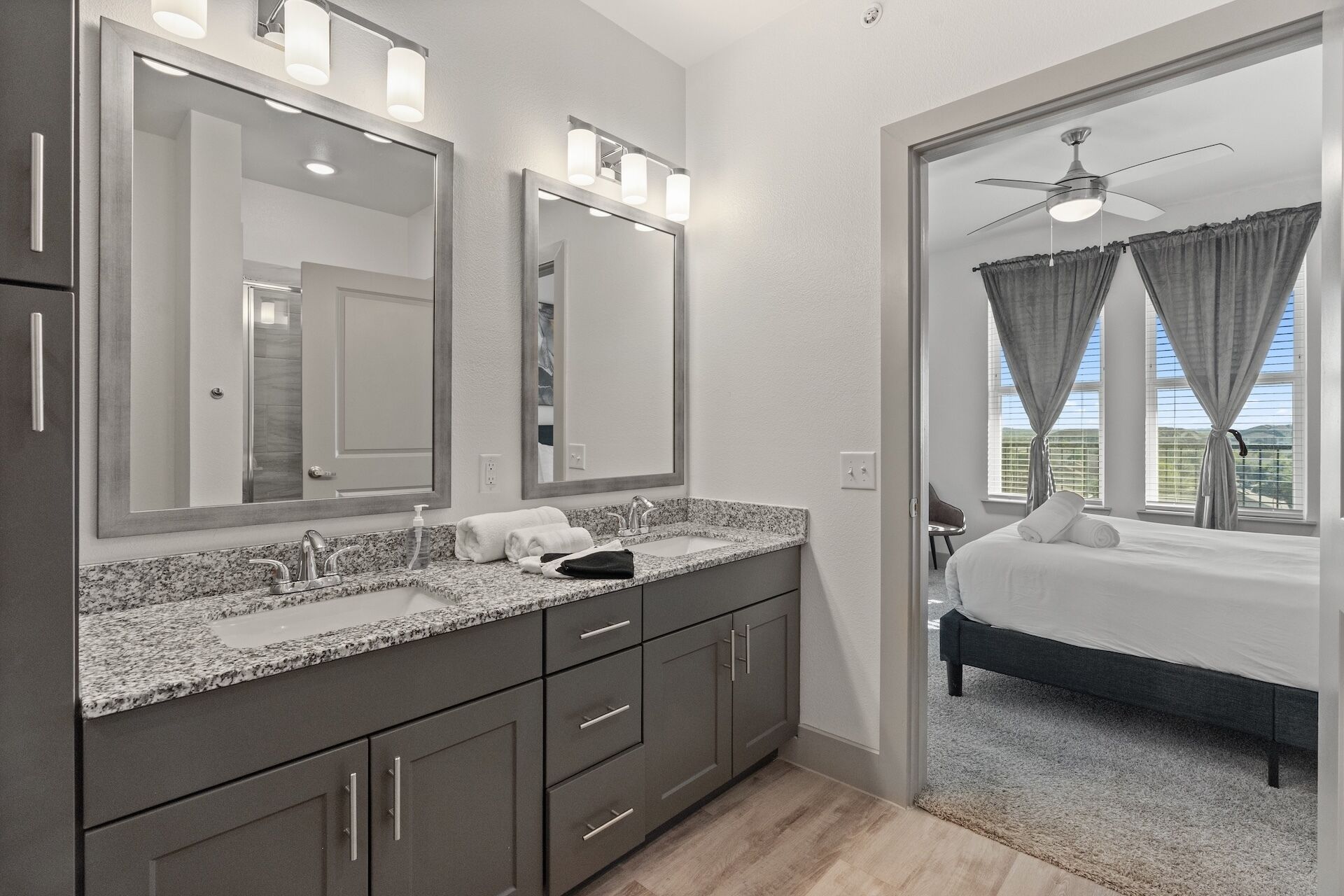 A modern bathroom with a double sink, large mirrors, and a ceiling fan.