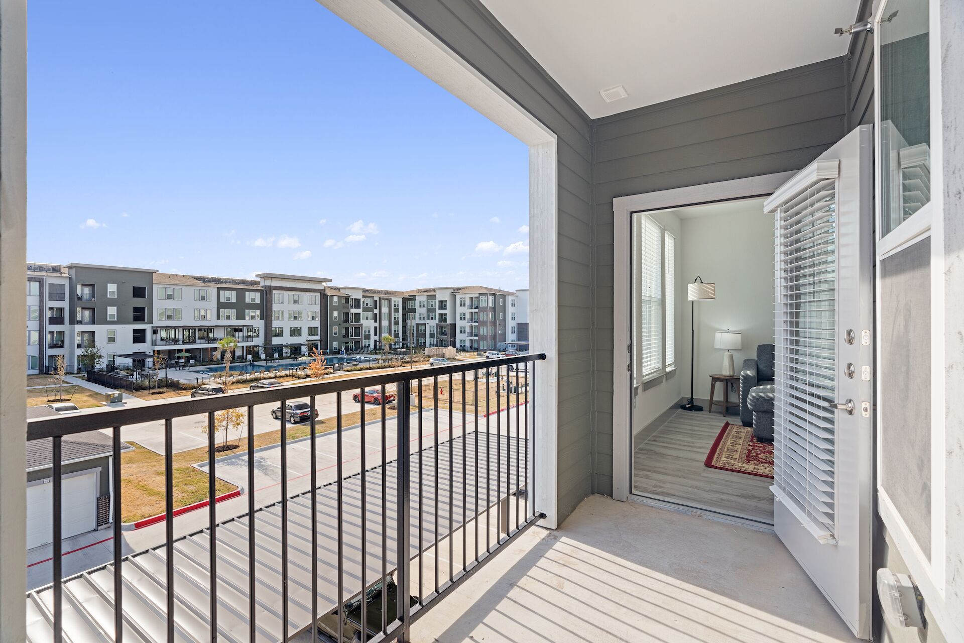 Un balcón con vista a un complejo residencial, un estacionamiento y una puerta que da a un espacio interior.