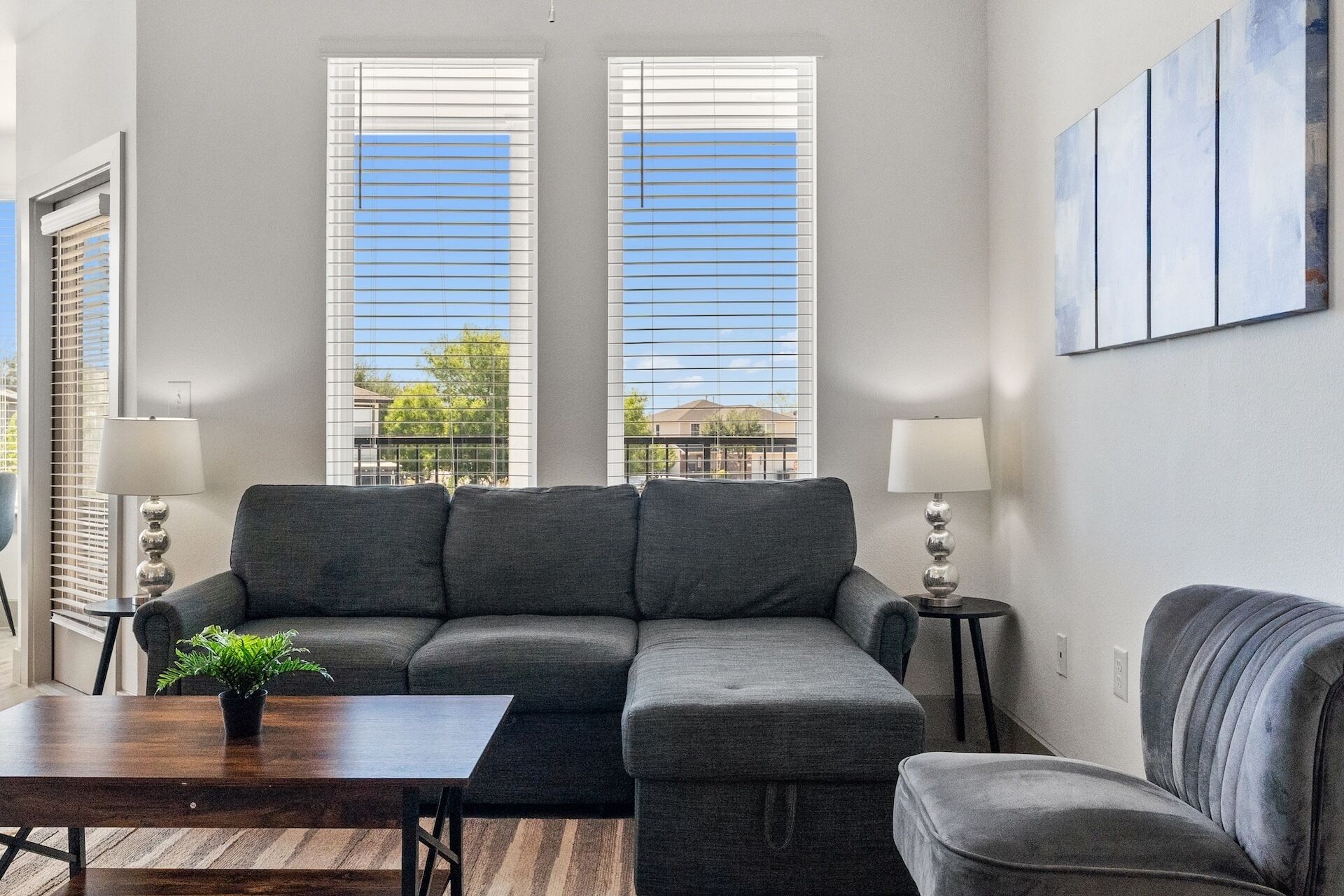 Una sala de estar con un sofá modular, dos mesas auxiliares con lámparas, una mesa de centro y una planta en maceta.