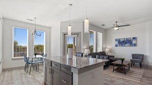 Une cuisine moderne dotée de plans de travail en granit, un coin repas avec une table et des chaises, et un salon avec un canapé et une table basse.