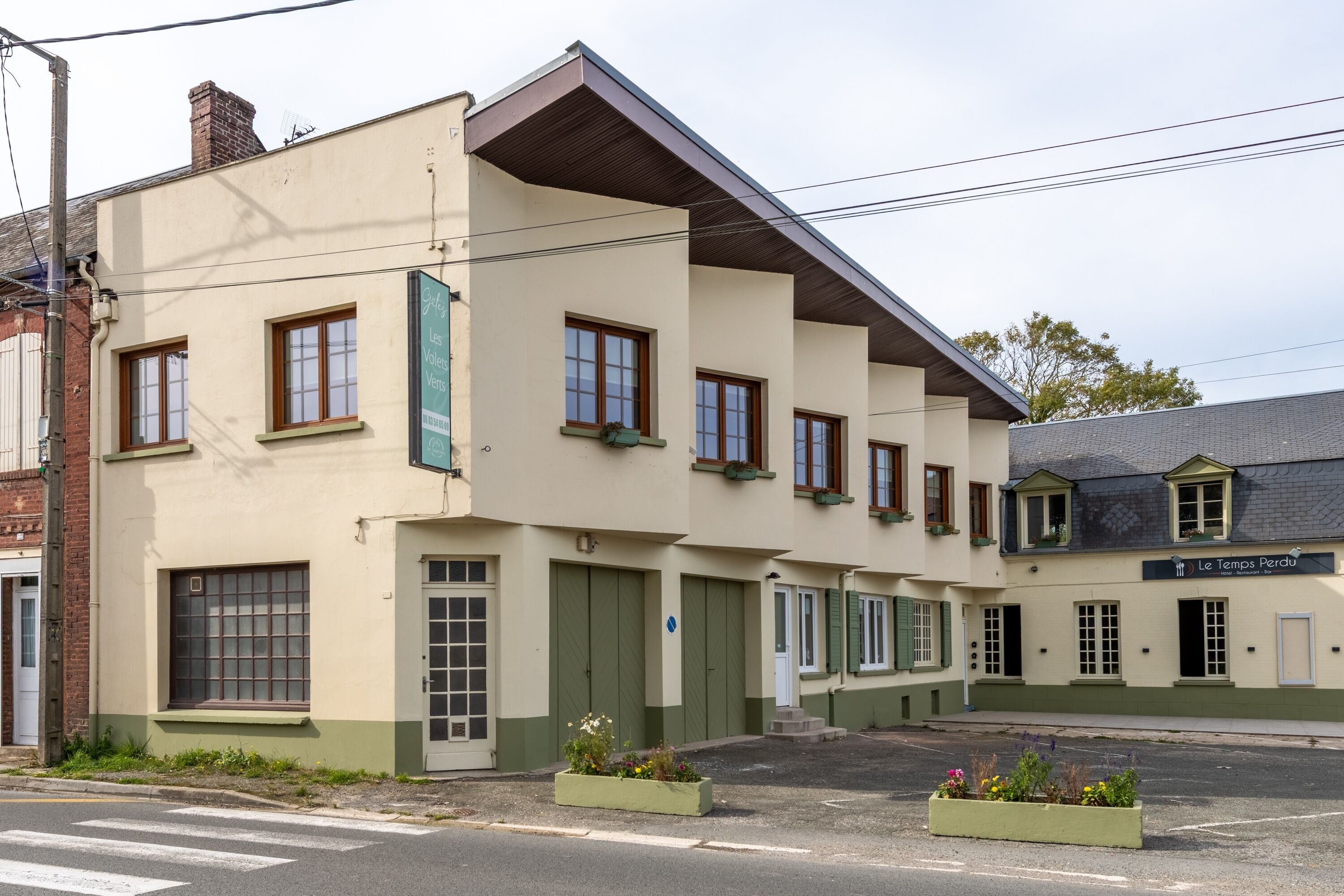 Ein zweistöckiges Gebäude mit grüner Fassade, mehreren Fenstern und einem Schild, auf dem "Le Temps Perdu" steht.