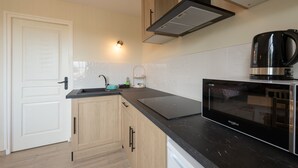 A modern kitchen with wooden cabinets, a black countertop, a built-in microwave, and a kettle.